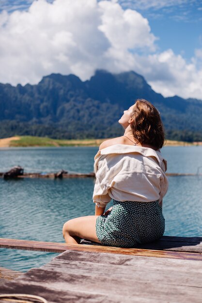 Donna in abito estivo e giacca turistica viaggia in Thailandia, parco nazionale di Khao Sok, splendida vista sulle barche e sul lago.