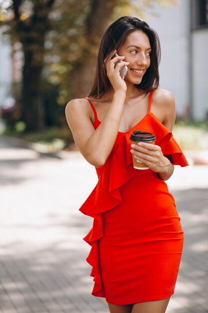 Donna in abito rosso utilizzando il telefono e bere caffè