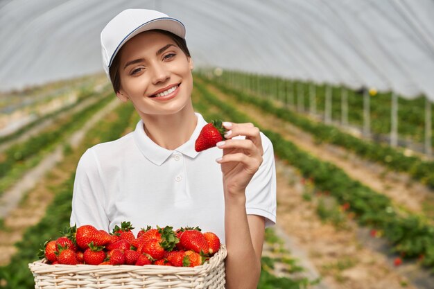 Donna in berretto bianco che tiene cesto con fragole mature