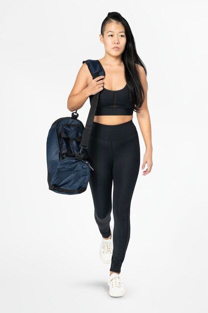 Donna in buona salute in abiti sportivi neri che trasportano il corpo pieno della borsa da palestra