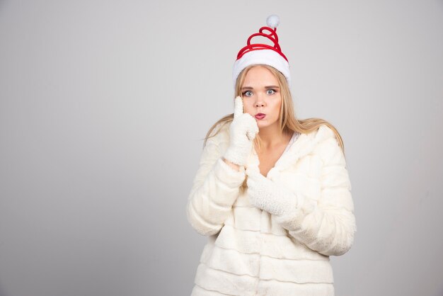 Donna in camice bianco e cappello di Babbo Natale in piedi sul muro grigio.