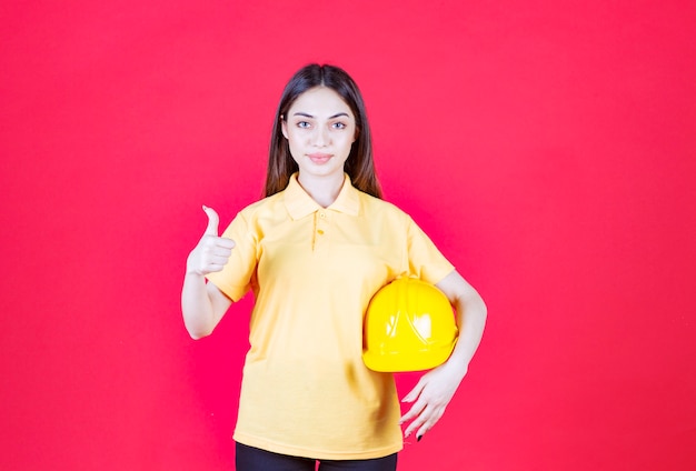 donna in camicia gialla che tiene un casco giallo e si gode il prodotto.