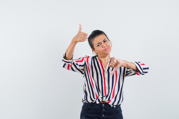 donna in camicia, gonna che mostra i pollici su e giù e sembra indecisa