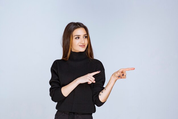 donna in camicia nera che indica qualcosa a destra.