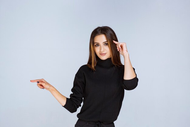 donna in camicia nera che punta a sinistra e mostra le sue emozioni.