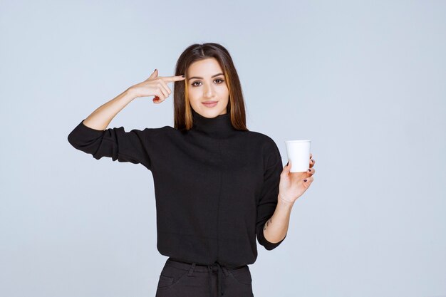 donna in camicia nera che tiene una tazza di caffè e pensa a nuove idee.