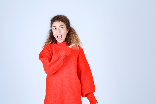 donna in camicia rossa che punta a qualcuno o da qualche parte con la faccia emotiva sul blu.