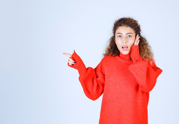 donna in camicia rossa che punta a qualcuno o da qualche parte con la faccia emotiva sul blu.