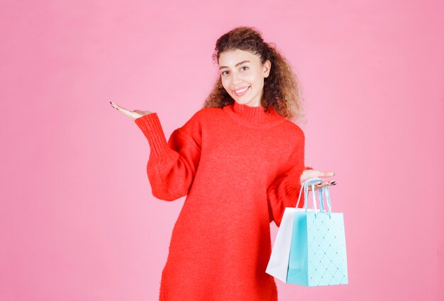 donna in camicia rossa che tiene più borse della spesa colorate.