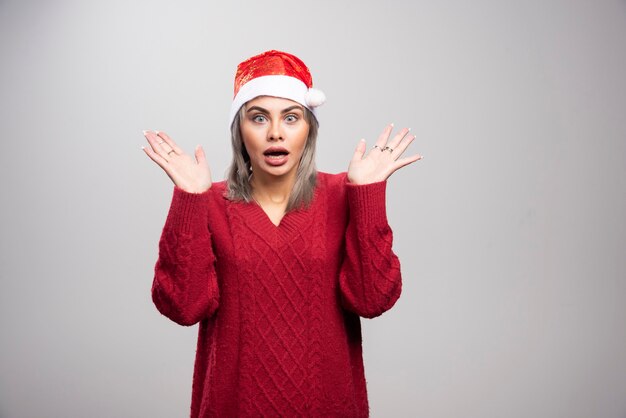 Donna in cappello di Babbo Natale che agisce sorpreso su sfondo grigio.