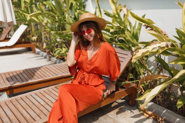 Donna in cappello di paglia e tuta arancione che riposa sulla sua villa durante le vacanze a Bali.