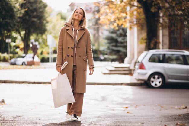 Donna in cappotto beige con la borsa della spesa in strada