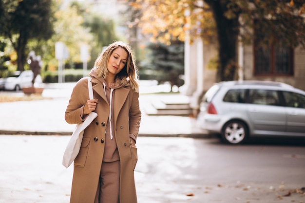 Donna in cappotto beige con la borsa della spesa in strada