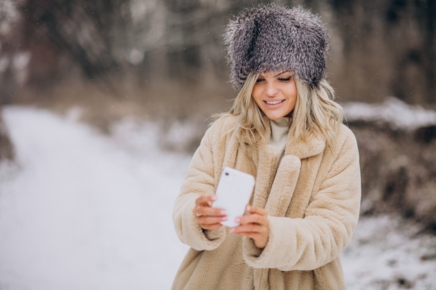 Donna in cappotto invernale che cammina nel parco pieno di neve parlando al telefono