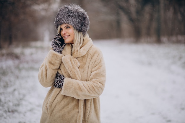 Donna in cappotto invernale che cammina nel parco pieno di neve parlando al telefono