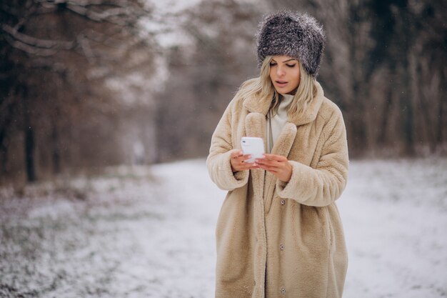 Donna in cappotto invernale che cammina nel parco pieno di neve parlando al telefono