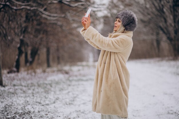 Donna in cappotto invernale che cammina nel parco pieno di neve parlando al telefono