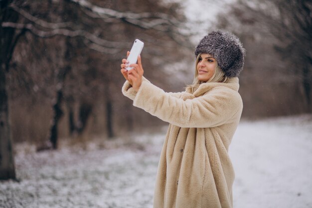 Donna in cappotto invernale che cammina nel parco pieno di neve parlando al telefono