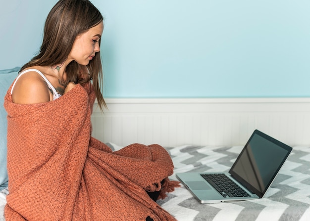 Donna in coperta a casa che lavora al computer portatile durante la pandemia