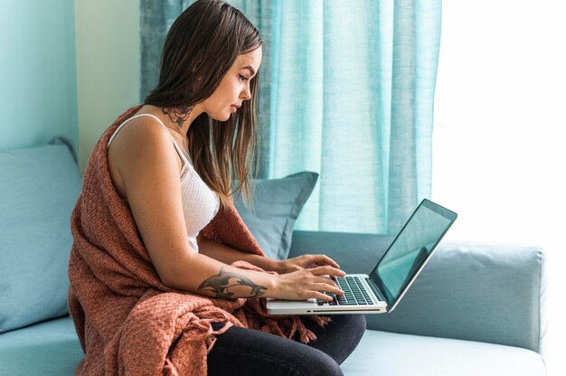 Donna in coperta a casa durante la pandemia lavorando sul computer portatile