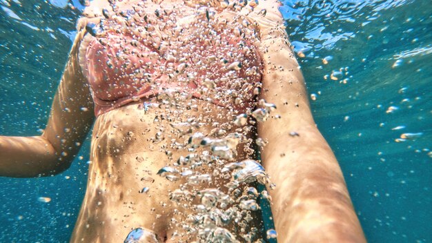 Donna in costume da bagno arancione nell'acqua blu e trasparente del Mar Mediterraneo. Tenendo la fotocamera