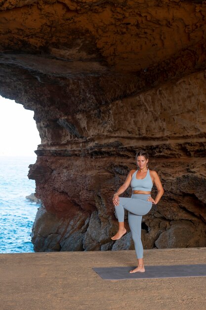 Donna in forma a tutto campo che fa yoga in riva al mare