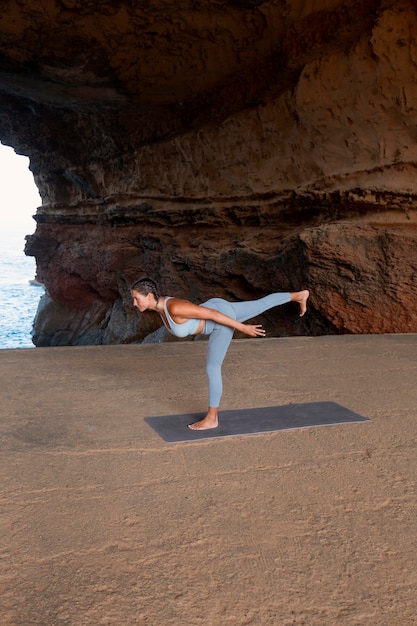 Donna in forma a tutto campo che fa yoga in riva al mare