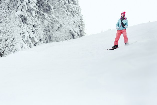 Donna in giacca da sci blu e pantaloni rosa scende sulla collina innevata sul suo snowboard