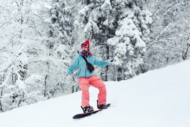 Donna in giacca da sci blu e pantaloni rosa si trova sullo snowboard da qualche parte nella foresta invernale