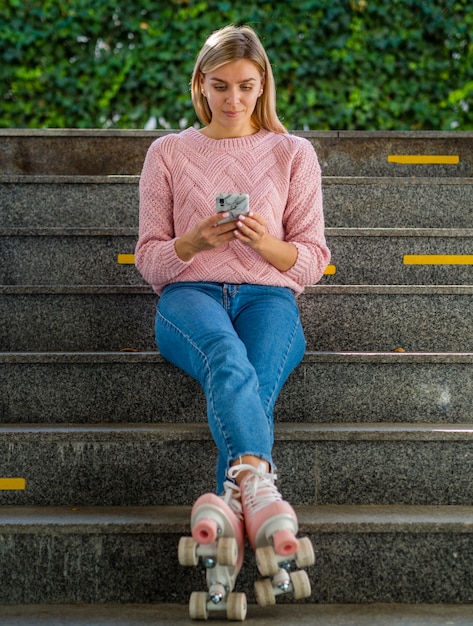 Donna in jeans e pattini a rotelle che esaminano smartphone