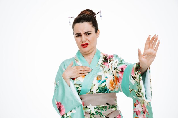 Donna in kimono giapponese tradizionale che guarda con un'espressione disgustata che fa un gesto di arresto alzando le mani su bianco