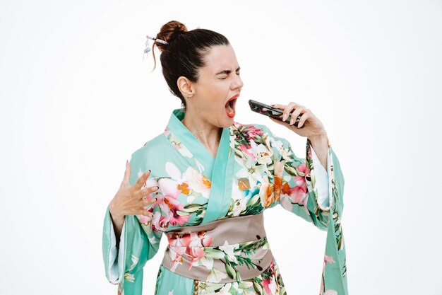 Donna in kimono giapponese tradizionale che tiene smartphone gridando di essere eccitata su bianco