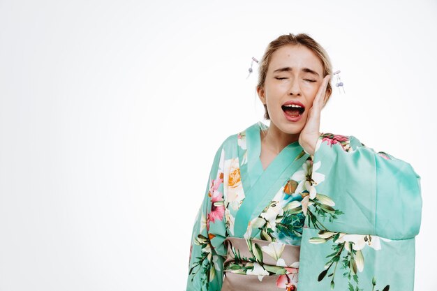 Donna in kimono tradizionale giapponese che sembra indisposta urlando toccandosi la guancia sentendo dolore con mal di denti su bianco