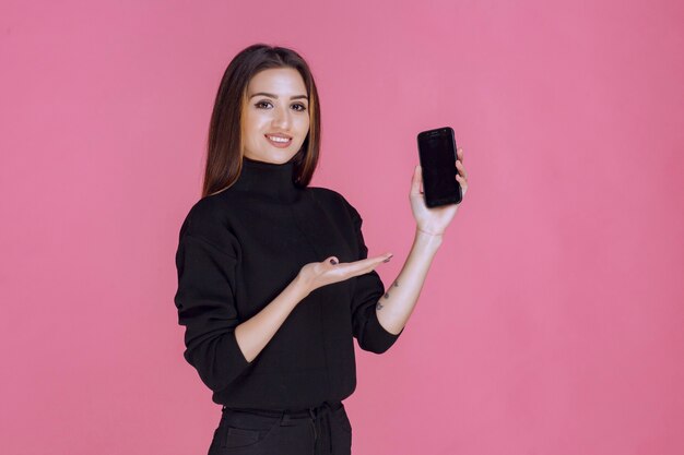 Donna in maglione nero che tiene uno smartphone.