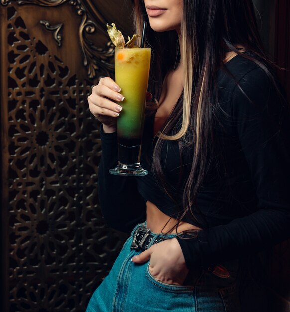 donna in piedi e in possesso di cocktail colorati al bar