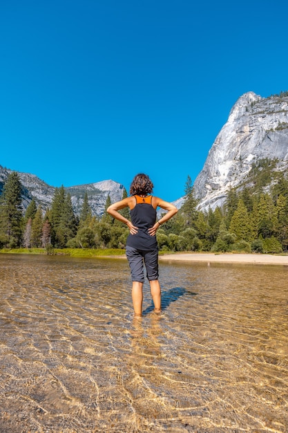 Donna in piedi nell'acqua di fronte alle montagne del Parco Nazionale di Yosemite