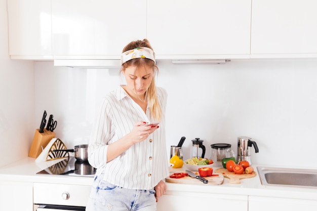 Donna in piedi vicino al piano di lavoro della cucina utilizzando il telefono cellulare