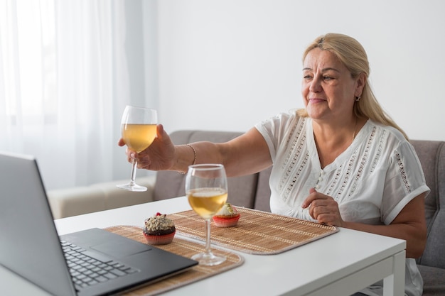 Donna in quarantena a casa con un drink con gli amici sul computer portatile