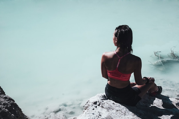 Donna in reggiseno sportivo rosa che si siede sulla roccia vicino al corpo d'acqua durante il giorno