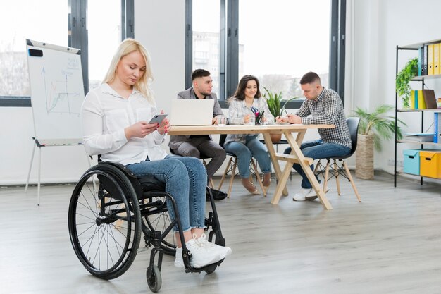 Donna in sedia a rotelle che lavora dal suo telefono all'ufficio