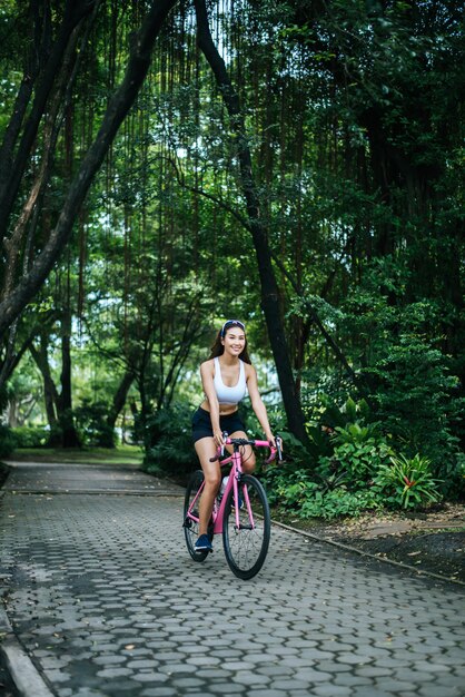 Donna in sella a una bici da strada nel parco. Ritratto di giovane donna bella sulla bici rosa.