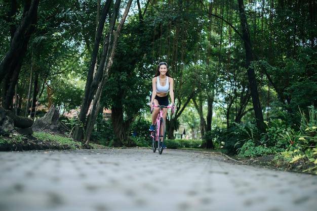 Donna in sella a una bici da strada nel parco. Ritratto di giovane donna bella sulla bici rosa.