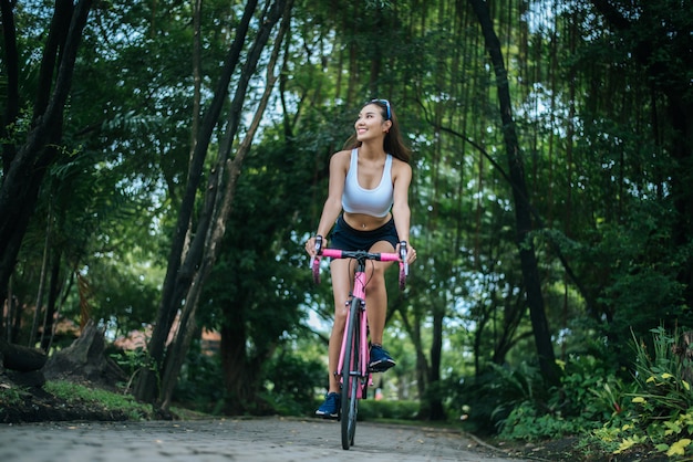 Donna in sella a una bici da strada nel parco. Ritratto di giovane donna bella sulla bici rosa.