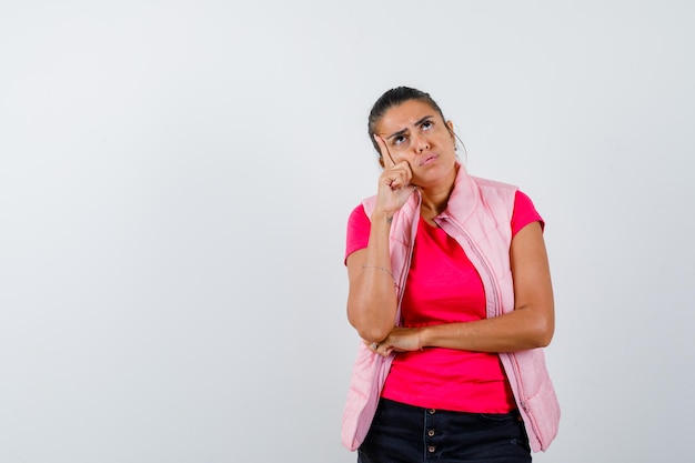 Donna in t-shirt, gilet in piedi in posa pensante e sembra esitante