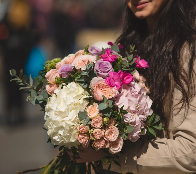 Donna in trench in possesso di un bouquet misto di fiori d'inverno.