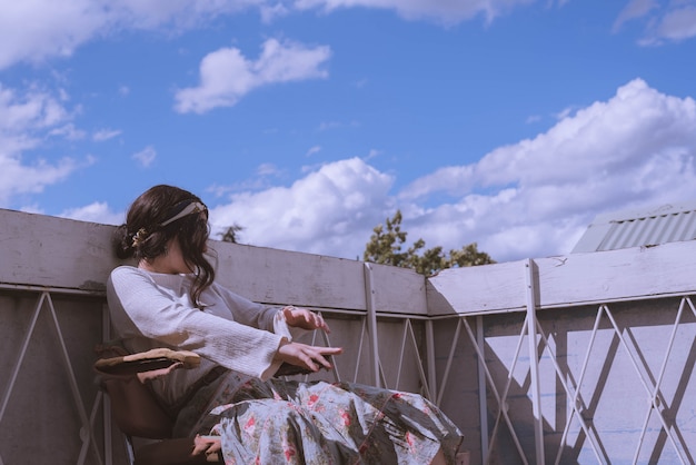 Donna in un abito vintage seduto sul tetto di un edificio con un bel cielo azzurro e nuvole