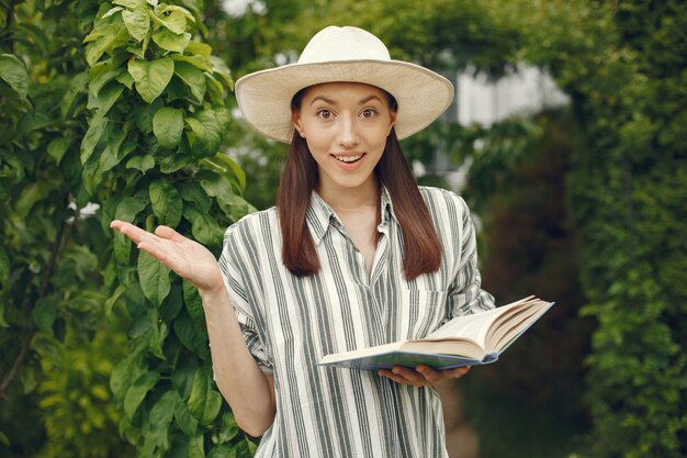 Donna in un cappello con un libro in un giardino