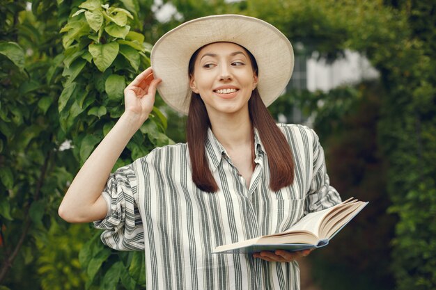 Donna in un cappello con un libro in un giardino