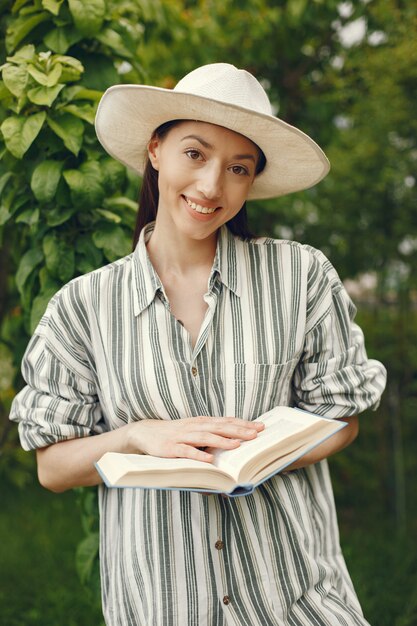 Donna in un cappello con un libro in un giardino