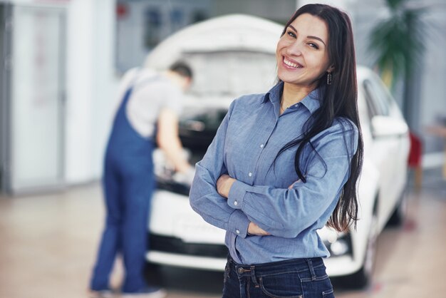 Donna in un garage auto ottenere assistenza meccanica. Il meccanico lavora sotto il cofano della macchina